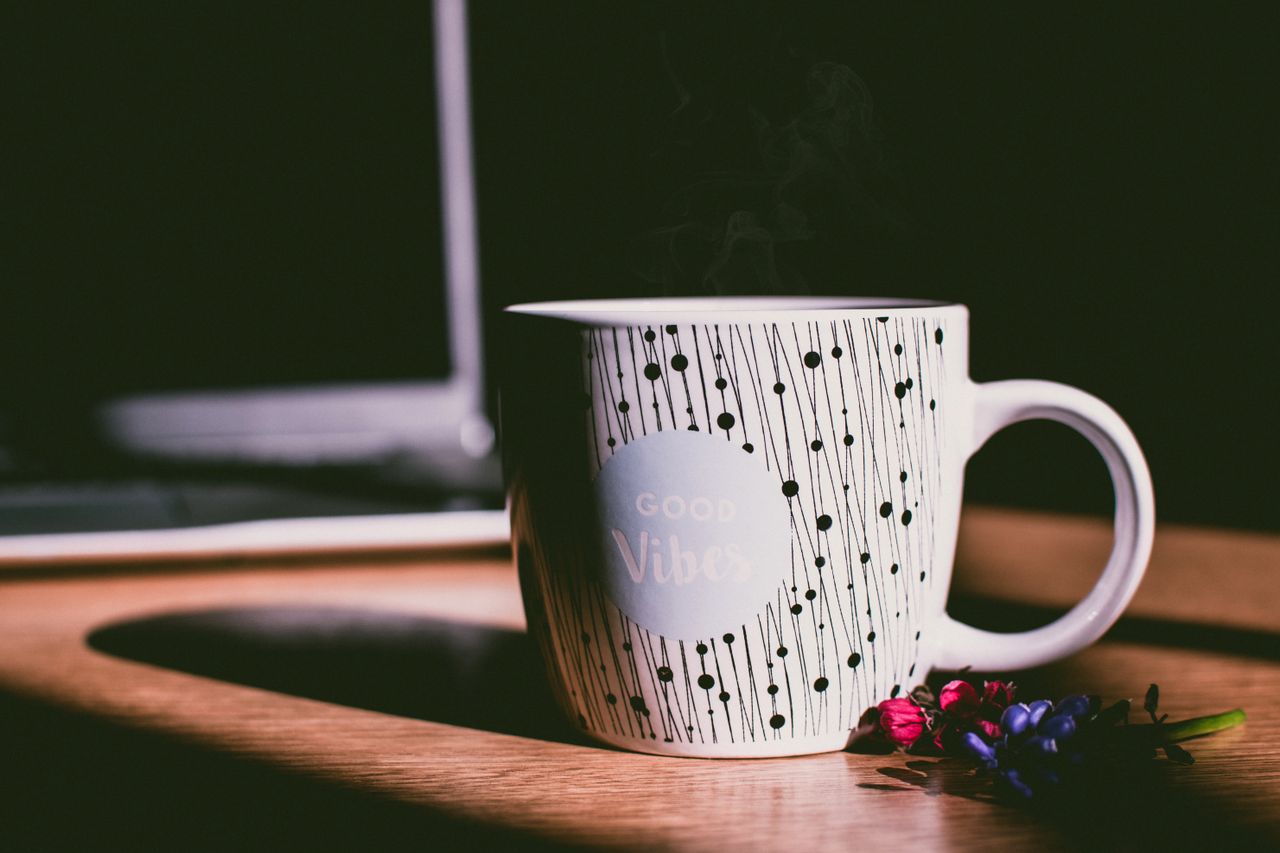 A stylish mug with 'Good Vibes' text, placed on a wooden desk with vibrant flowers.