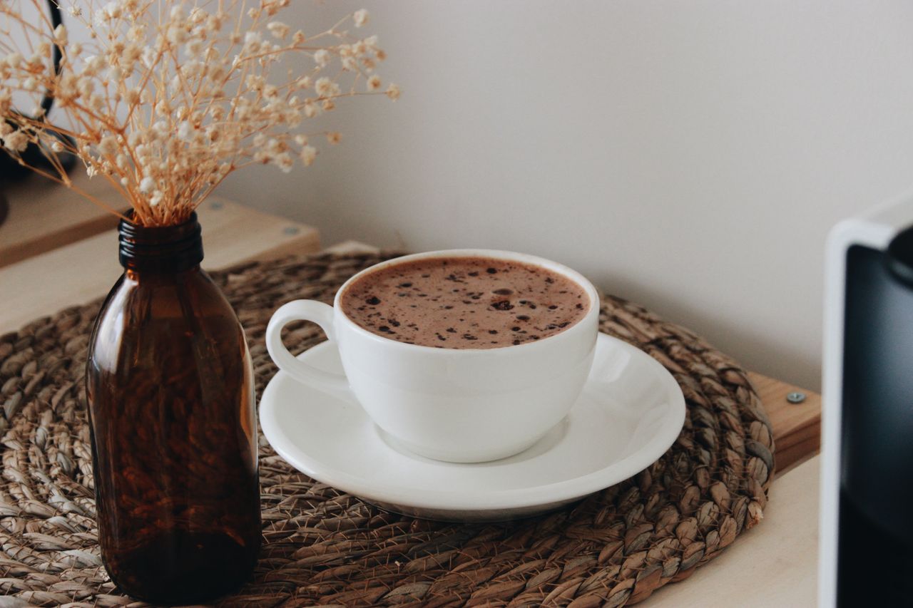 Enjoy a cozy cup of hot chocolate on a rustic woven placemat beside dried flowers in an amber bottle.