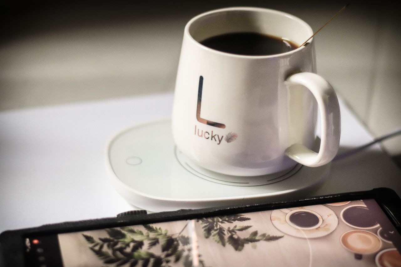 A cozy scene with a mug of black coffee on a wireless charger next to a smartphone.